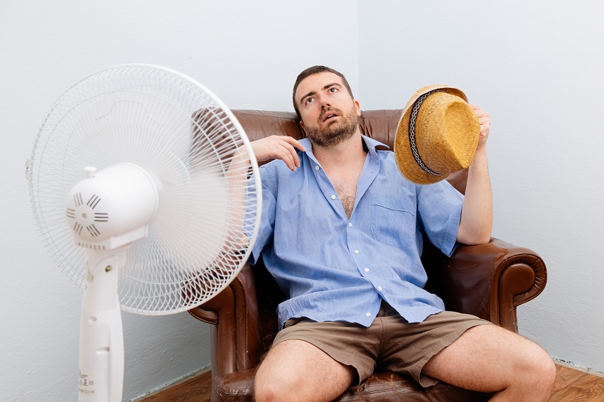 Мужчина пытается справиться с жарой при помощи вентилятора